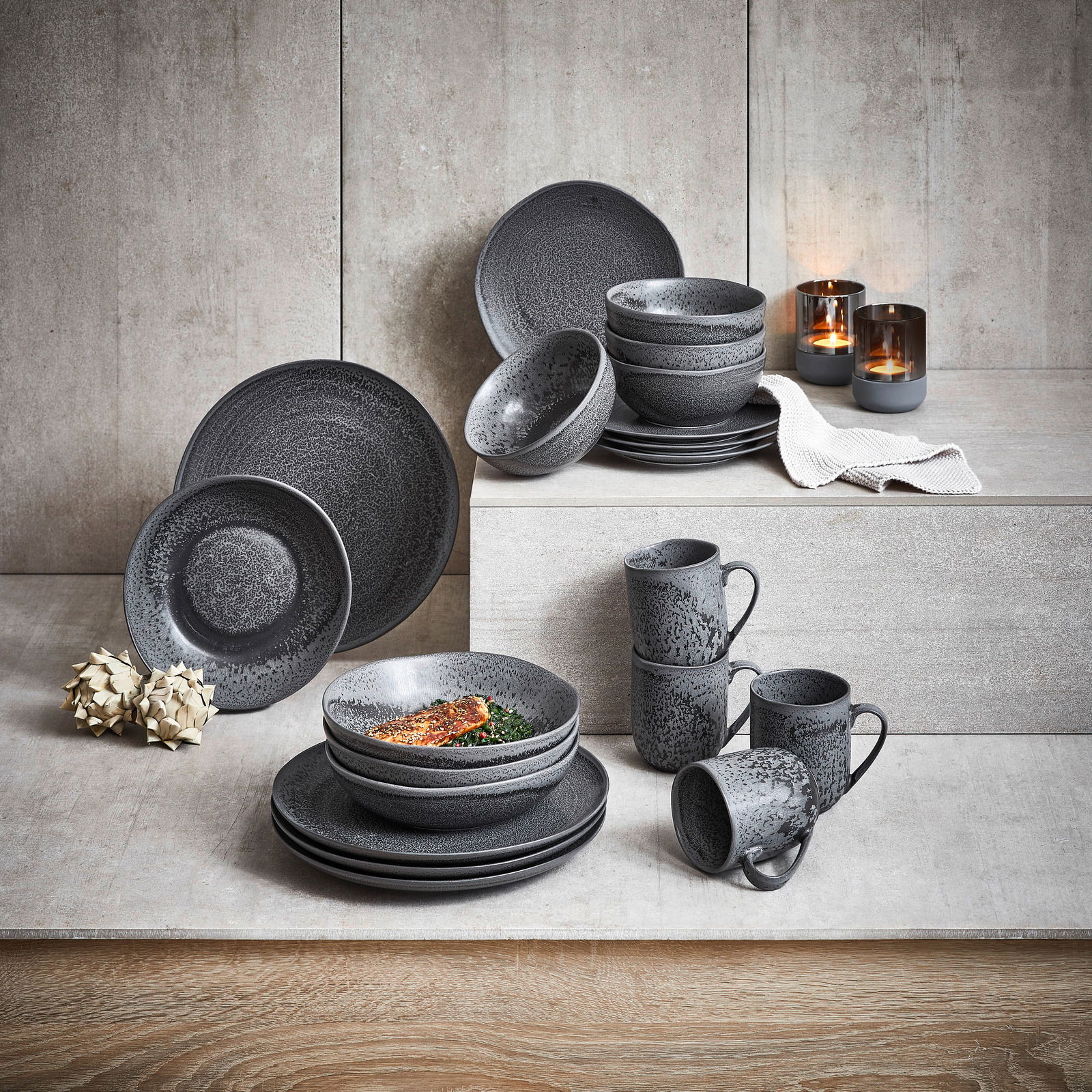 Kombiservice 20-teilig in stilvollem, dunklem Design, bestehend aus Tellern, Schalen und Tassen, präsentiert auf einer gestuften Betonoberfläche mit Kerzen im Hintergrund.
