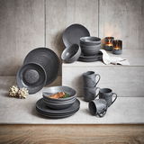 Kombiservice 20-teilig in stilvollem, dunklem Design, bestehend aus Tellern, Schalen und Tassen, präsentiert auf einer gestuften Betonoberfläche mit Kerzen im Hintergrund.