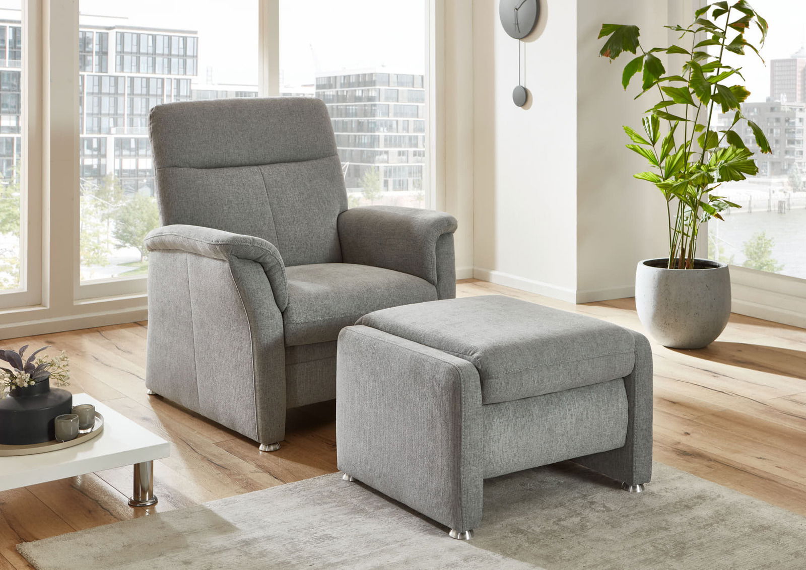 Grauer Sessel mit passendem Hocker in einem modernen Wohnzimmer, seitliche Perspektive.