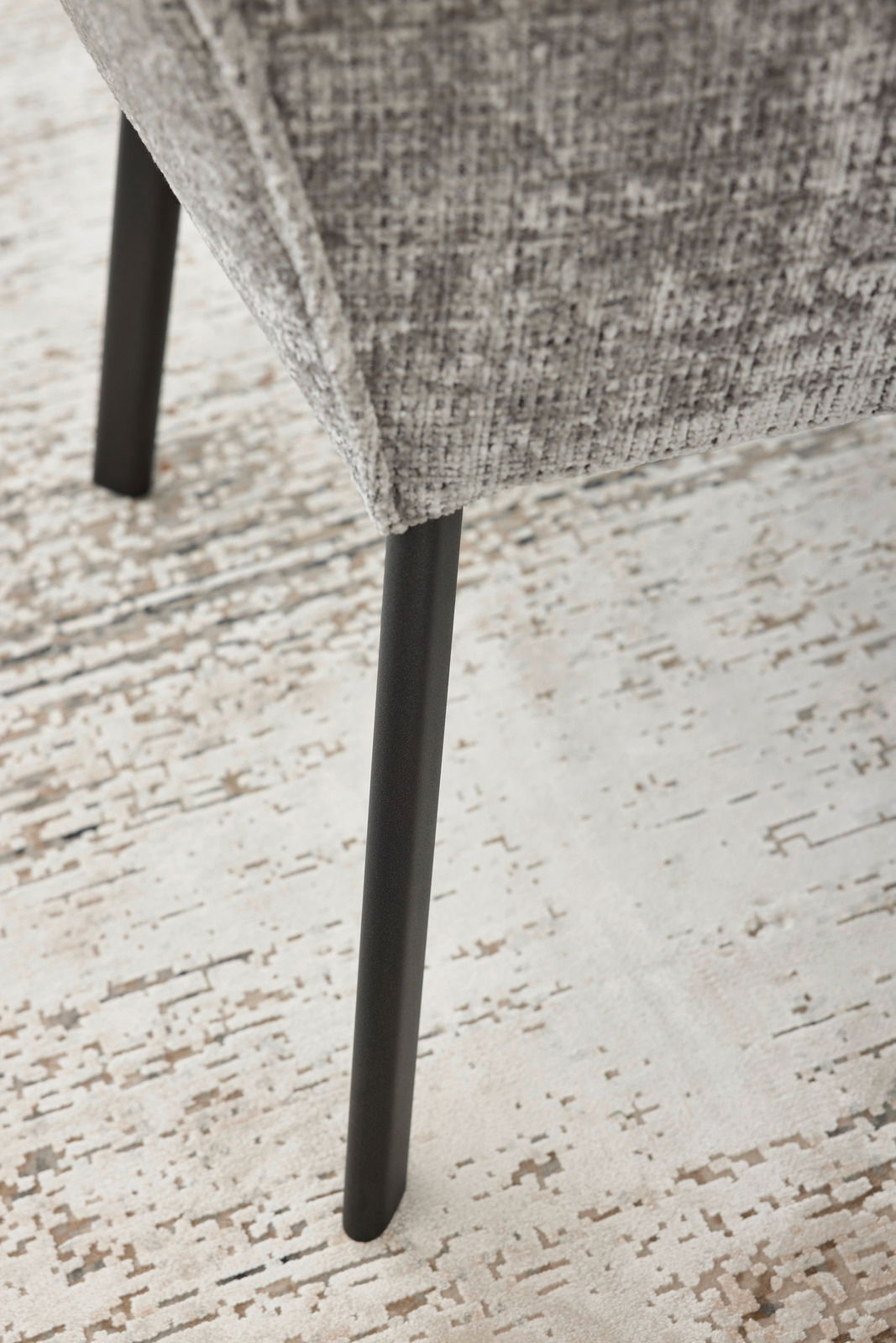 Nahaufnahme eines Armlehnstuhls mit grauem Stoffbezug und schwarzem Metallbein, seitliche Perspektive