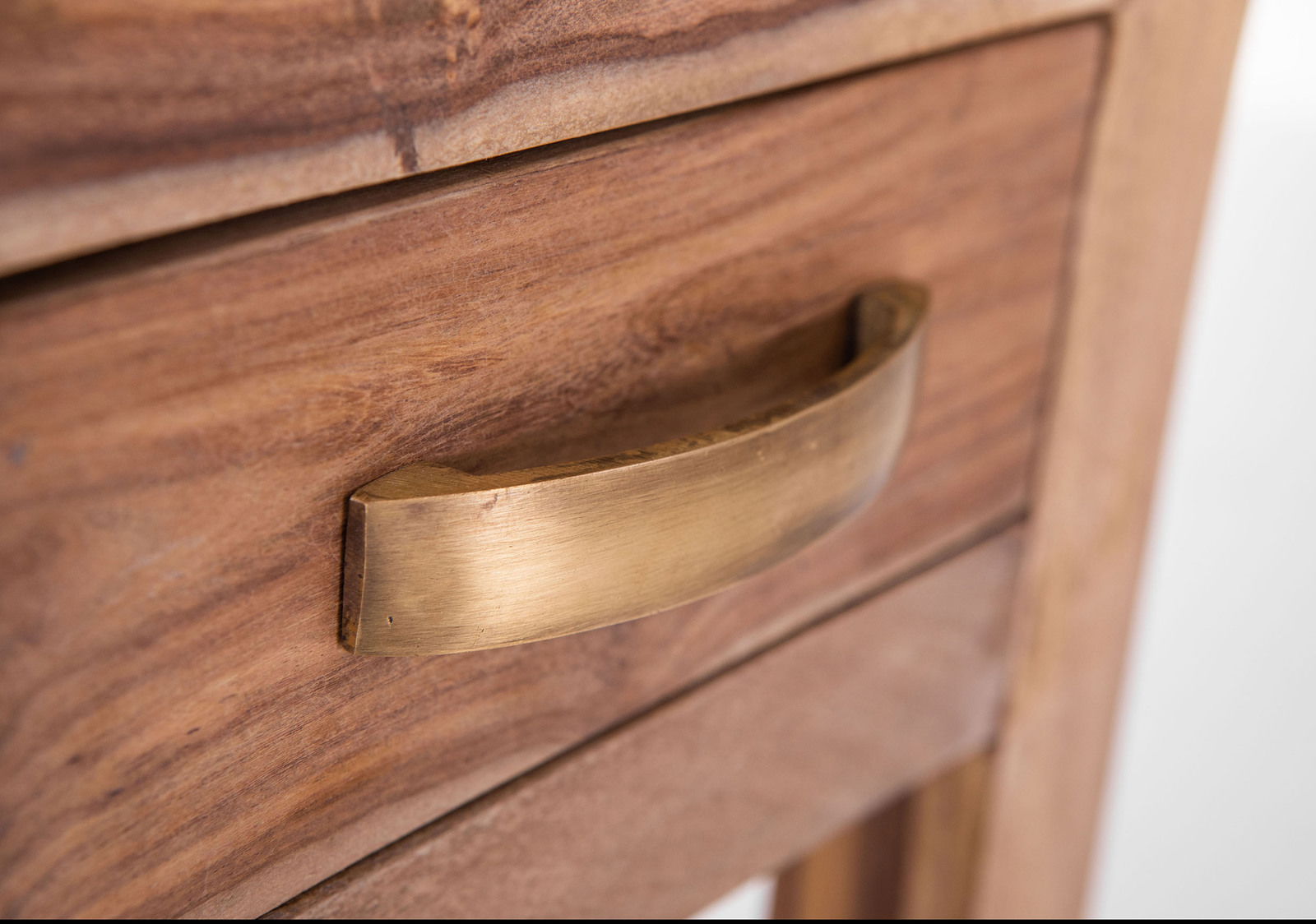 Nahaufnahme einer Holzschublade mit einem gebogenen, goldfarbenen Griff, seitliche Perspektive.