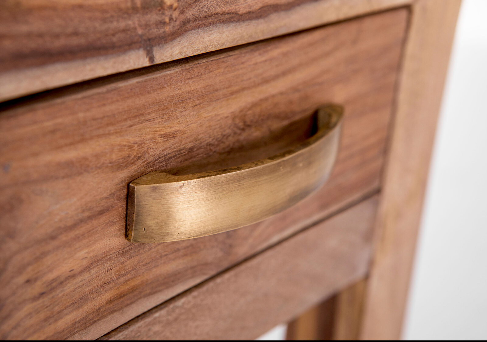 Nahaufnahme einer Holzschublade mit einem gebogenen, goldfarbenen Griff, seitliche Perspektive.
