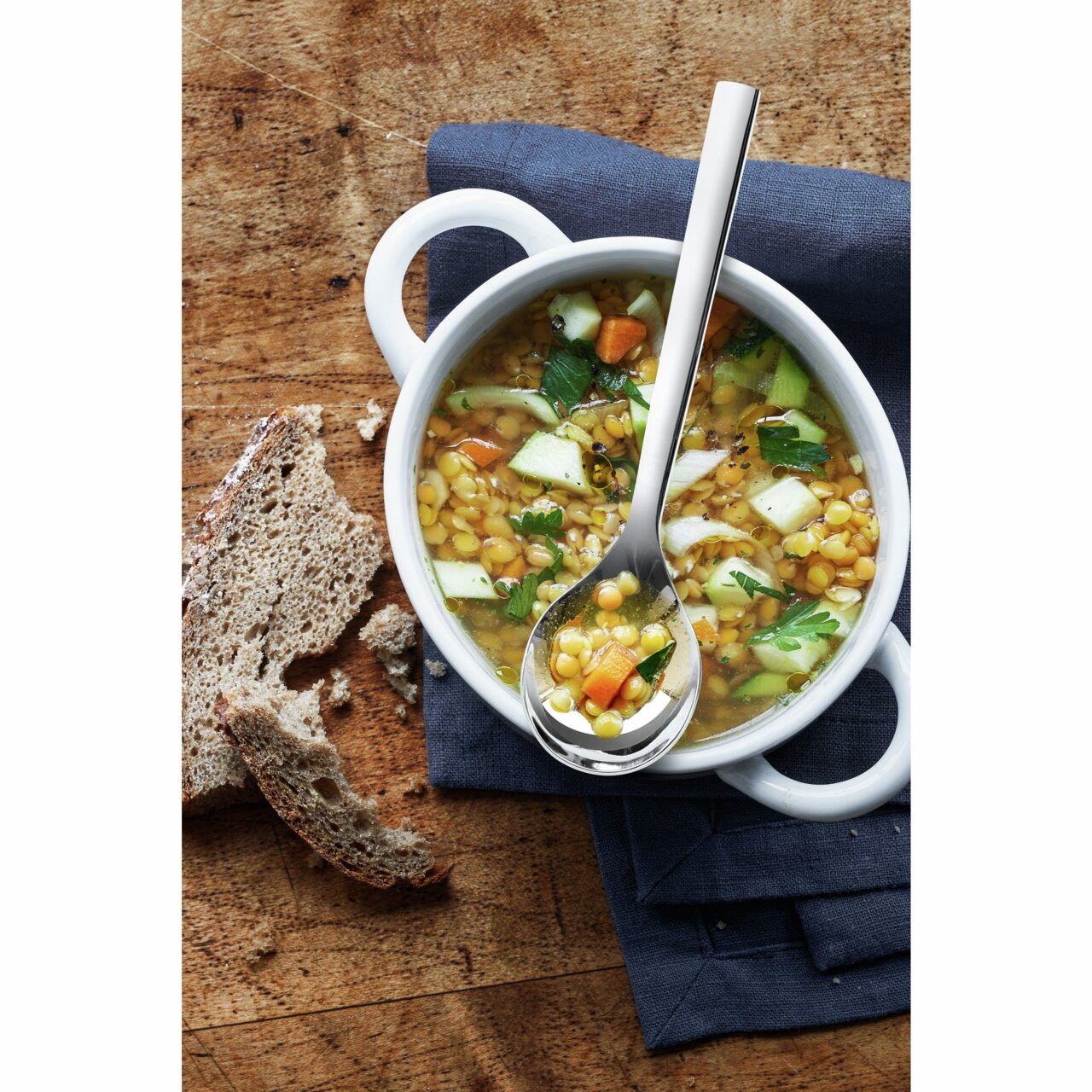 Suppentassenlöffel aus Edelstahl in einer weißen Suppenschale mit Linsensuppe, von oben fotografiert.