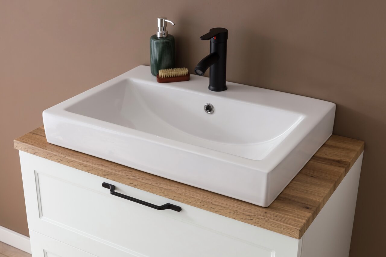 Moderner Waschtisch mit weißem Keramikbecken, schwarzer Armatur und Holzplatte, aus der Vogelperspektive fotografiert.