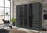 Moderner 5-türiger Drehtürenschrank in dunklem Design, frontal abgebildet in einem stilvollen Raum mit Backsteinwand und großen Fenstern.