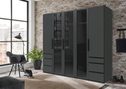 Moderner 5-türiger Drehtürenschrank in dunklem Design, frontal abgebildet in einem stilvollen Raum mit Backsteinwand und großen Fenstern.