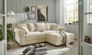 Gemütliche beige Rundecke in einem hellen Wohnzimmer mit großen Fenstern, dekoriert mit Kissen und einer Decke, aus der Perspektive von vorne links.