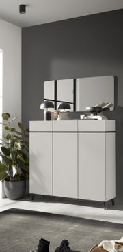 Frontale Ansicht eines modernen, hohen Sideboards in Hellgrau mit drei Schubladen, drei Türen, schwarzen Akzentlinien und schlanken Metallfüßen, stilvoll mit Spiegel, Leuchten und Wohnaccessoires inszeniert.