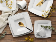 Vogelperspektive auf ein elegantes, weißes Kombiservice-Set mit quadratischen Tellern, Tassen und goldfarbenem Besteck auf einem Holztisch, dekoriert mit gelben Blumen und Eukalyptusblättern.