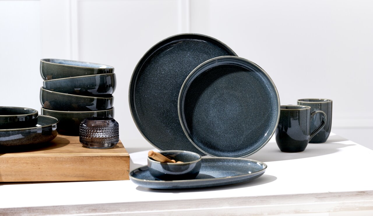 Verschiedene dunkelgraue Keramikteller und Schalen in einem modernen Design, seitlich von oben fotografiert.