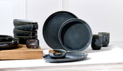 Verschiedene dunkelgraue Keramikteller und Schalen in einem modernen Design, seitlich von oben fotografiert.