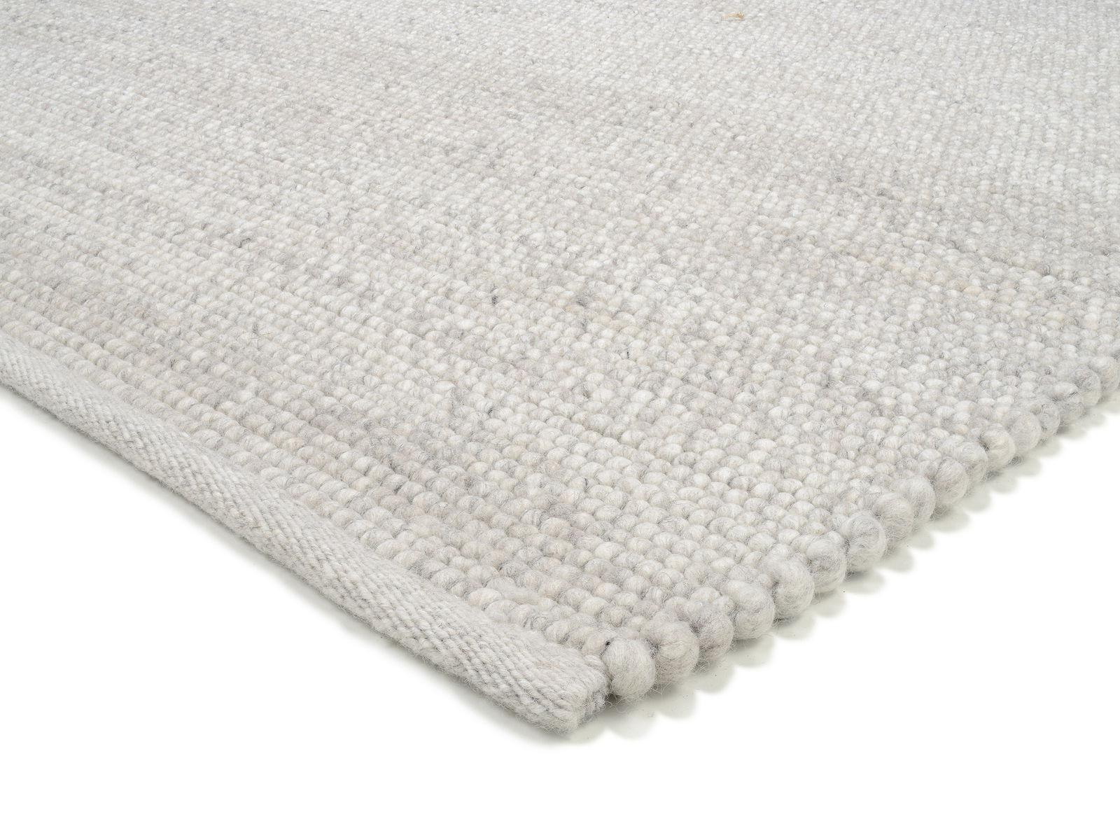 Nahaufnahme eines handgewebten Teppichs in hellem Grau mit strukturierter Oberfläche, perspektivisch von der Seite aufgenommen.