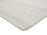 Nahaufnahme eines handgewebten Teppichs in hellem Grau mit strukturierter Oberfläche, perspektivisch von der Seite aufgenommen.