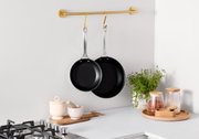 Twee zwarte 3-PLY-pannen, opgehangen aan een gouden stang in een moderne keuken, gezien vanuit de zijkant.