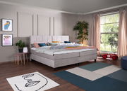 Modernes Boxspringbett in einem stilvoll eingerichteten Schlafzimmer mit großen Fenstern und dekorativen Elementen, seitliche Perspektive.