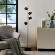 Schwarze Stehleuchte mit vier kugelförmigen, kupferfarben spiegelnden Lampenköpfen im modernen Wohnzimmer neben Sessel und Sideboard, frontale Perspektive