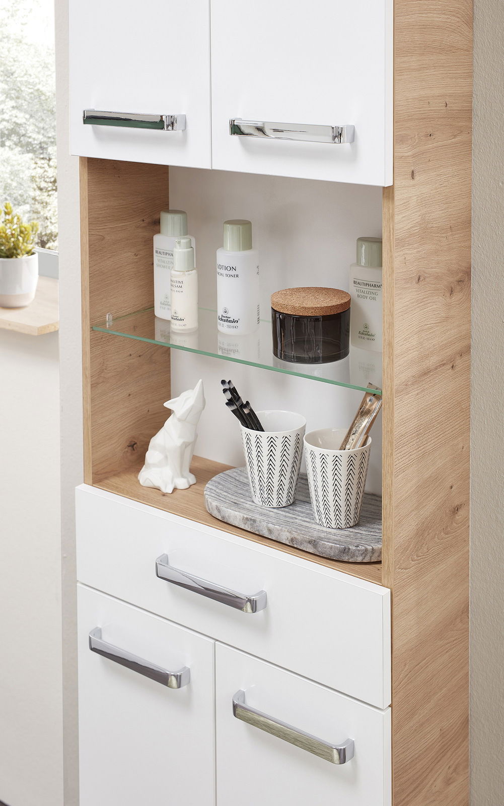 Hochschrank mit weißer Front und Holzoptik, offene Regale mit Pflegeprodukten und Dekoration, seitliche Perspektive