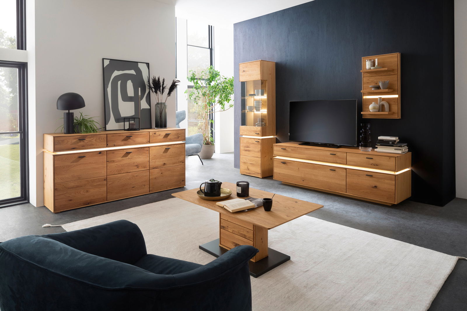 Moderne Wohnzimmermöbelkombination in Holzoptik mit LED-Beleuchtung, bestehend aus Sideboard, Highboard, Couchtisch und TV-Element, aus der Perspektive eines gemütlichen Wohnzimmers.