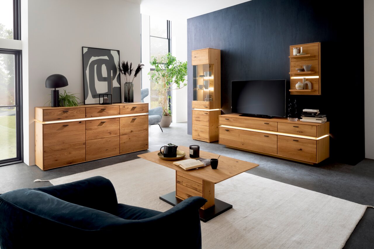 Moderne Wohnzimmermöbelkombination in Holzoptik mit LED-Beleuchtung, bestehend aus Sideboard, Highboard, Couchtisch und TV-Element, aus der Perspektive eines gemütlichen Wohnzimmers.