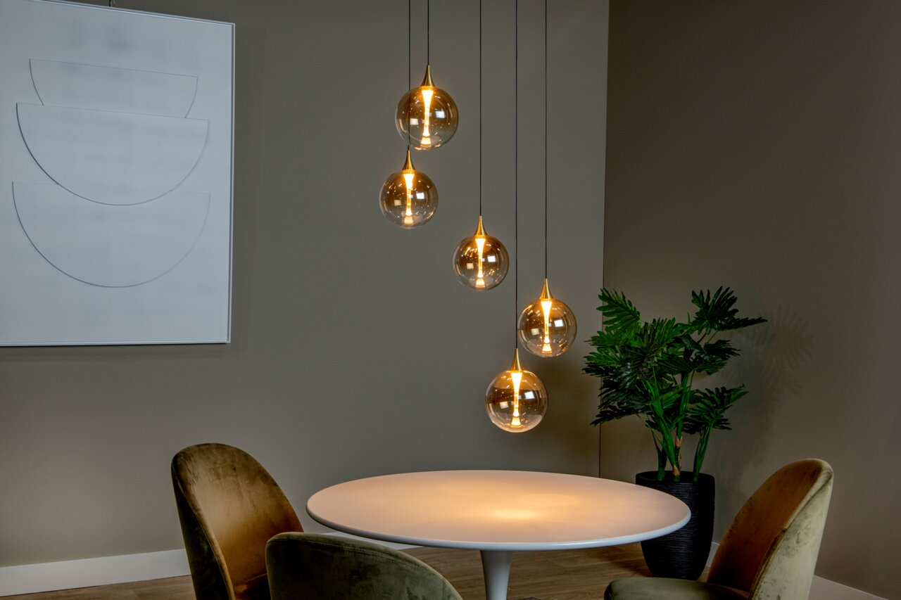 Moderne Hängeleuchte mit fünf kugelförmigen, transparenten Lampenschirmen, die in einem eleganten Esszimmer über einem runden Tisch hängen. Seitliche Perspektive.
