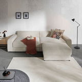 Beige Ecksofa mit Kissen und Decke, seitliche Perspektive, in modernem Wohnzimmer mit Stehlampe und Wanddekoration.