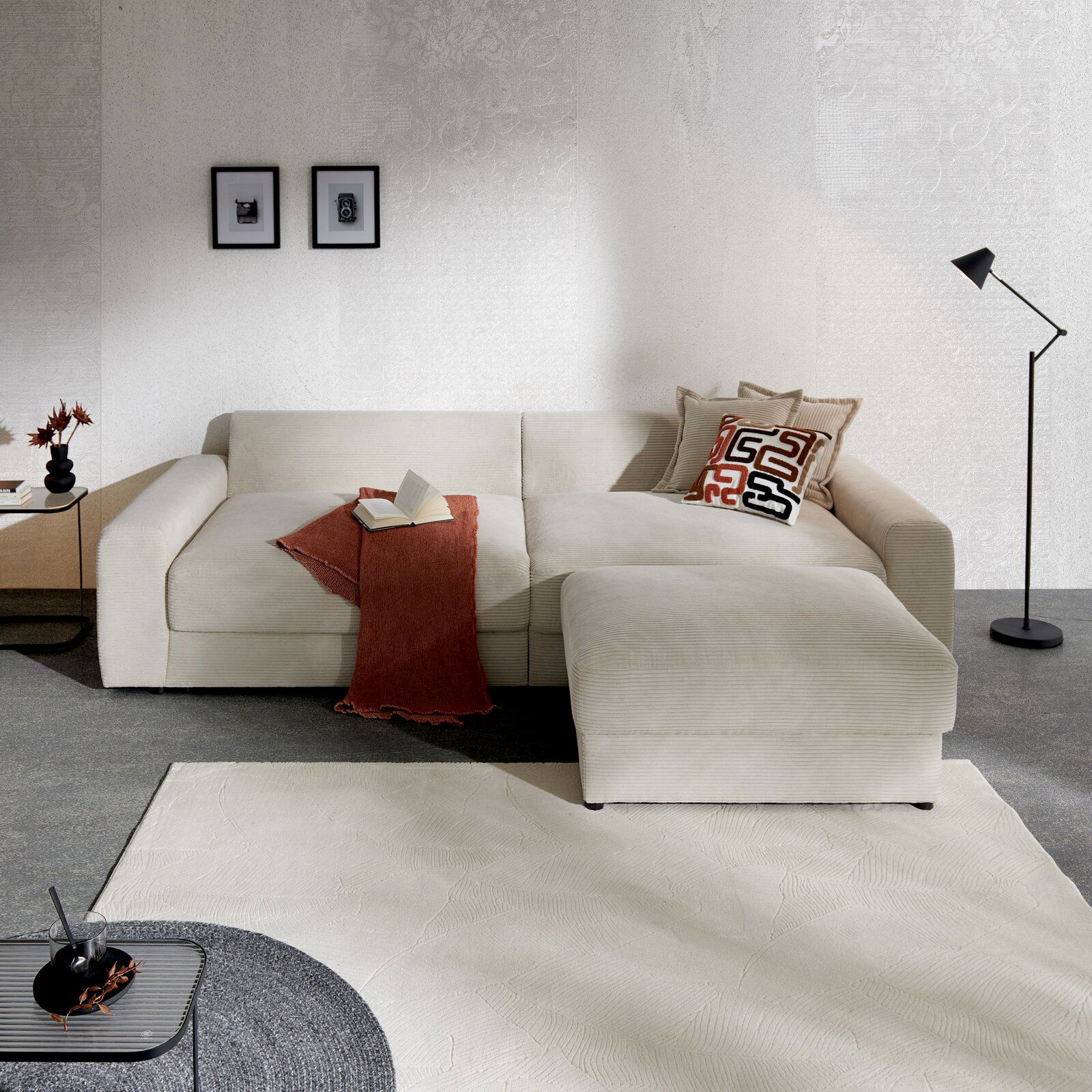 Beige Ecksofa mit Kissen und Decke, seitliche Perspektive, in modernem Wohnzimmer mit Stehlampe und Wanddekoration.