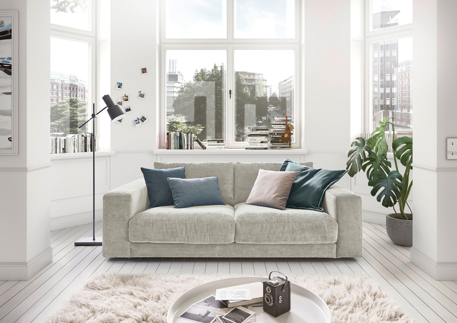 Lounge Handmade Sofa 2-Sitzer LH-SAMBIA Gemütliches 2-Sitzer-Sofa in einem hellen Wohnzimmer mit großen Fenstern, dekoriert mit Kissen in verschiedenen Farben, aus der Frontperspektive.