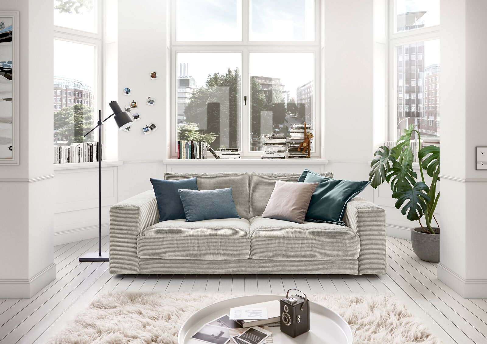 Gemütliches 2-Sitzer-Sofa in einem hellen Wohnzimmer mit großen Fenstern, dekoriert mit Kissen in verschiedenen Farben, aus der Frontperspektive.