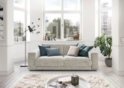Gemütliches 2-Sitzer-Sofa in einem hellen Wohnzimmer mit großen Fenstern, dekoriert mit Kissen in verschiedenen Farben, aus der Frontperspektive.