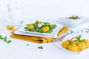 Schräg von vorn fotografierter Teller mit frischem Blattsalat und goldgelben Bällchen auf weißem Geschirr, dekoriert auf heller Tischdecke mit Besteck und gelbem Tuch.