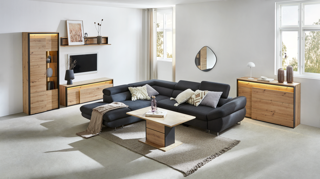 Hom´in Kommode Modernes Wohnzimmer mit einem schwarzen Ecksofa, einem Couchtisch aus Holz und Metall, einem TV-Lowboard, einem Highboard und einer Kommode aus Holz. Die Möbel sind in einem hellen Raum mit großen Fenstern und minimalistischer Dekoration platziert. Perspe