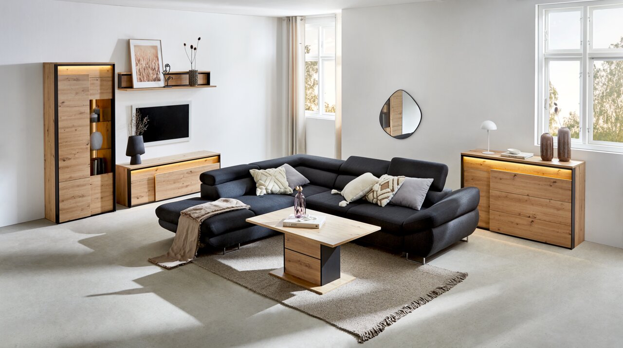 Modernes Wohnzimmer mit einem schwarzen Ecksofa, einem Couchtisch aus Holz und Metall, einem TV-Lowboard, einem Highboard und einer Kommode aus Holz. Die Möbel sind in einem hellen Raum mit großen Fenstern und minimalistischer Dekoration platziert. Perspe