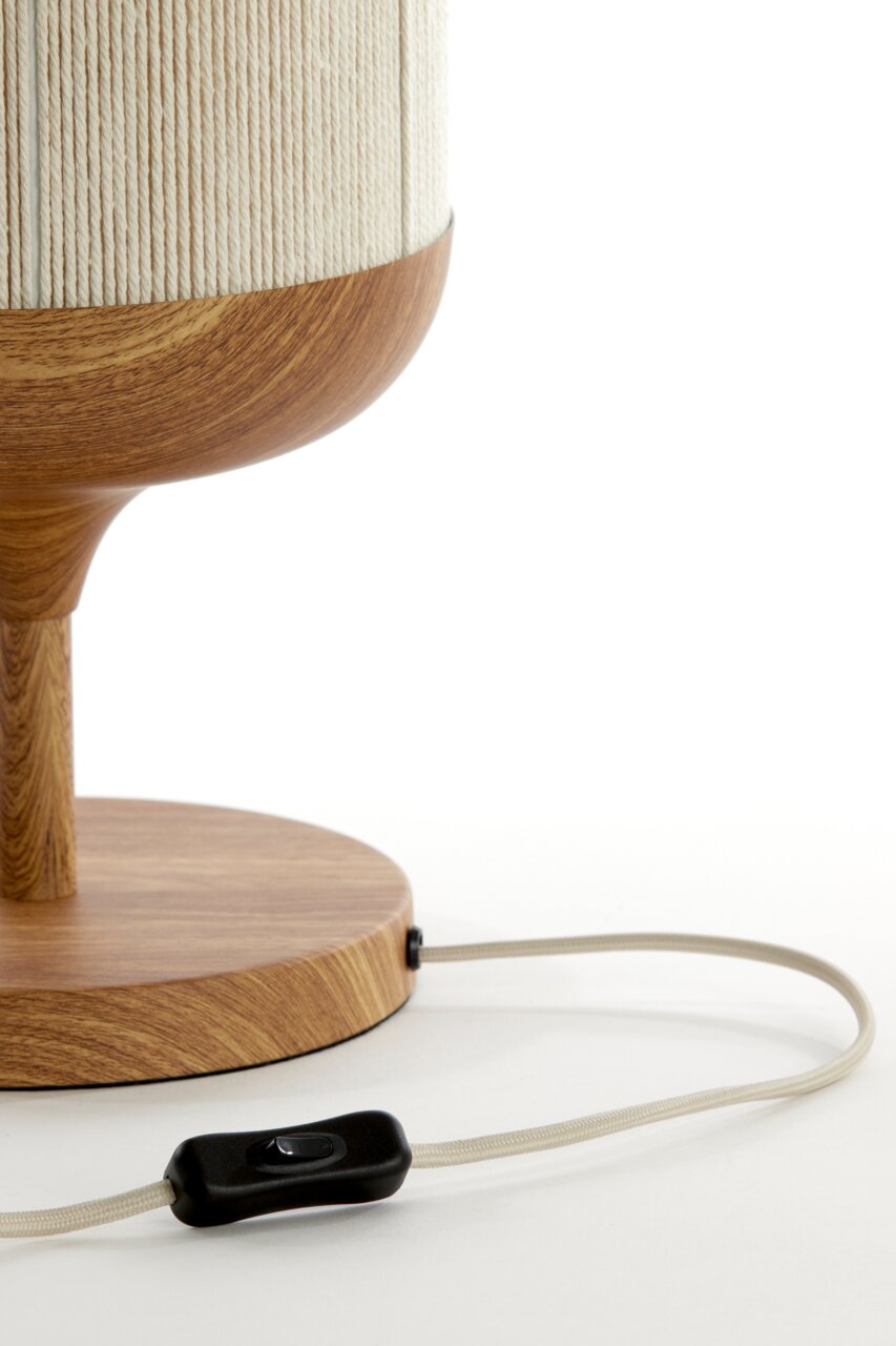 Detailfoto van een tafellamp met houten voet en houten sokkel, crèmekleurige lampenkap met structuur en stoffen snoer met zwarte tussenschakelaar, close-up van de zijkant