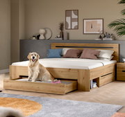 Modernes Holzbett in Eiche-Optik mit hohem Kopfteil, integrierten Schubladen und offenem Stauraum, im Schlafzimmer-Setting; Perspektive: frontale 3/4-Ansicht von links.