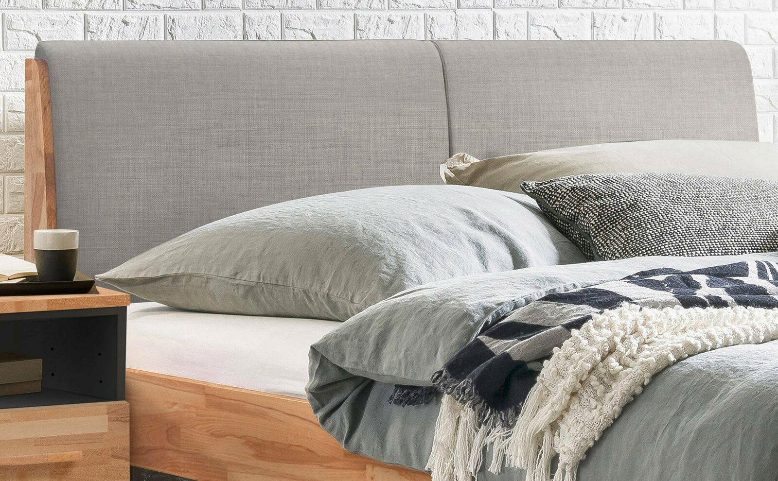 Nahaufnahme eines Bettgestells mit grauem Kopfteil und Holzelementen, seitliche Perspektive