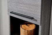 Detailaufnahme einer grauen Holzschublade mit schwarzem, länglichem Metallgriff; Perspektive schräg von vorn rechts, darunter offenes Fach mit rundem Holzdöschen