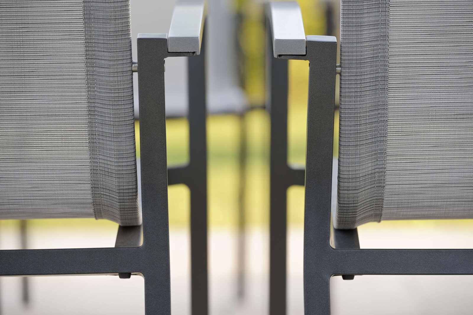 Close-up van twee grijze metalen stapelstoelen met armleuningen, gezien vanaf de zijkant.
