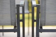 Close-up van twee grijze metalen stapelstoelen met armleuningen, gezien vanaf de zijkant.