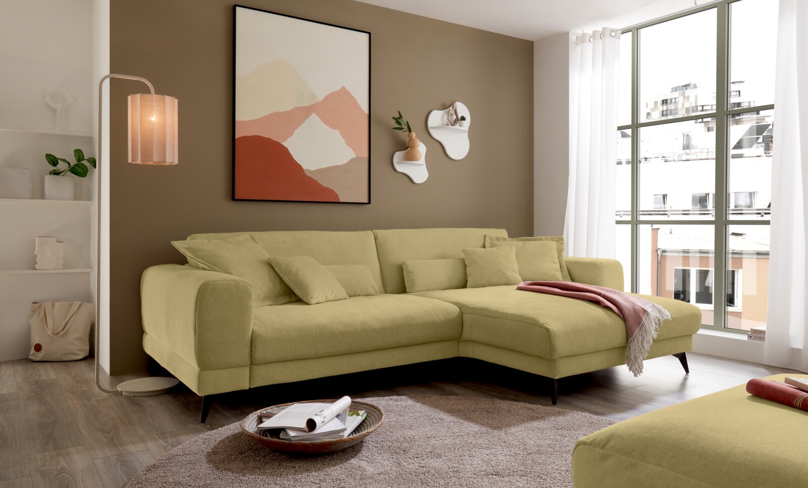 Set one by Musterring Ecksofa SET ONE MIDLAND Modernes hellgrünes Ecksofa mit Recamiere und Zierkissen im Wohnzimmer, seitliche Frontansicht leicht von links.