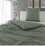 Grüne Wendebettwäsche auf einem Bett, fotografiert aus einer seitlichen Perspektive mit einem Kissen im Hintergrund.