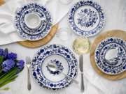 Dunkelblau-weißes Porzellan-Geschirrset mit floralem Dekor, Tellern und Tassen auf weißer Tischdecke mit Besteck, Holzuntersetzern, Glas und Blumen, fotografiert in Draufsicht von oben