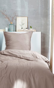 Bettwäsche-Set in Beige auf einem Bett, fotografiert aus der Frontperspektive, mit dekorativen Elementen im Hintergrund.