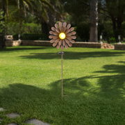 Solarleuchte in Form einer Blume mit gelbem Licht in der Mitte, aufgestellt in einem Garten. Frontalansicht.