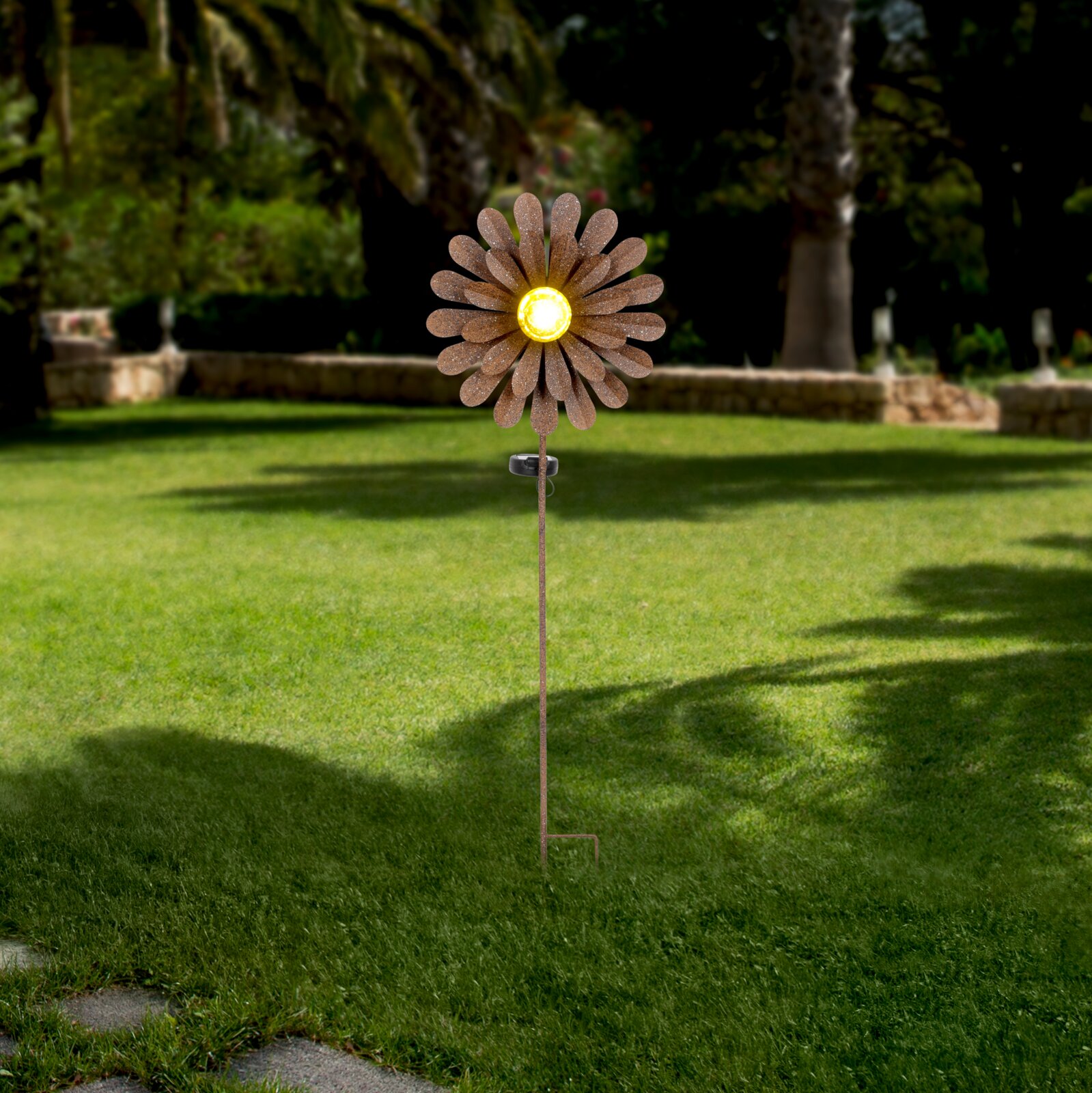 Ambia Garden Solarleuchte SOLARLEUCHTE Solarleuchte in Form einer Blume mit gelbem Licht in der Mitte, aufgestellt in einem Garten. Frontalansicht.