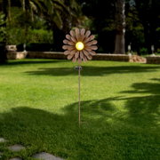 Zonne-lamp in de vorm van een bloem met geel licht in het midden, geplaatst in een tuin. Vooraanzicht.