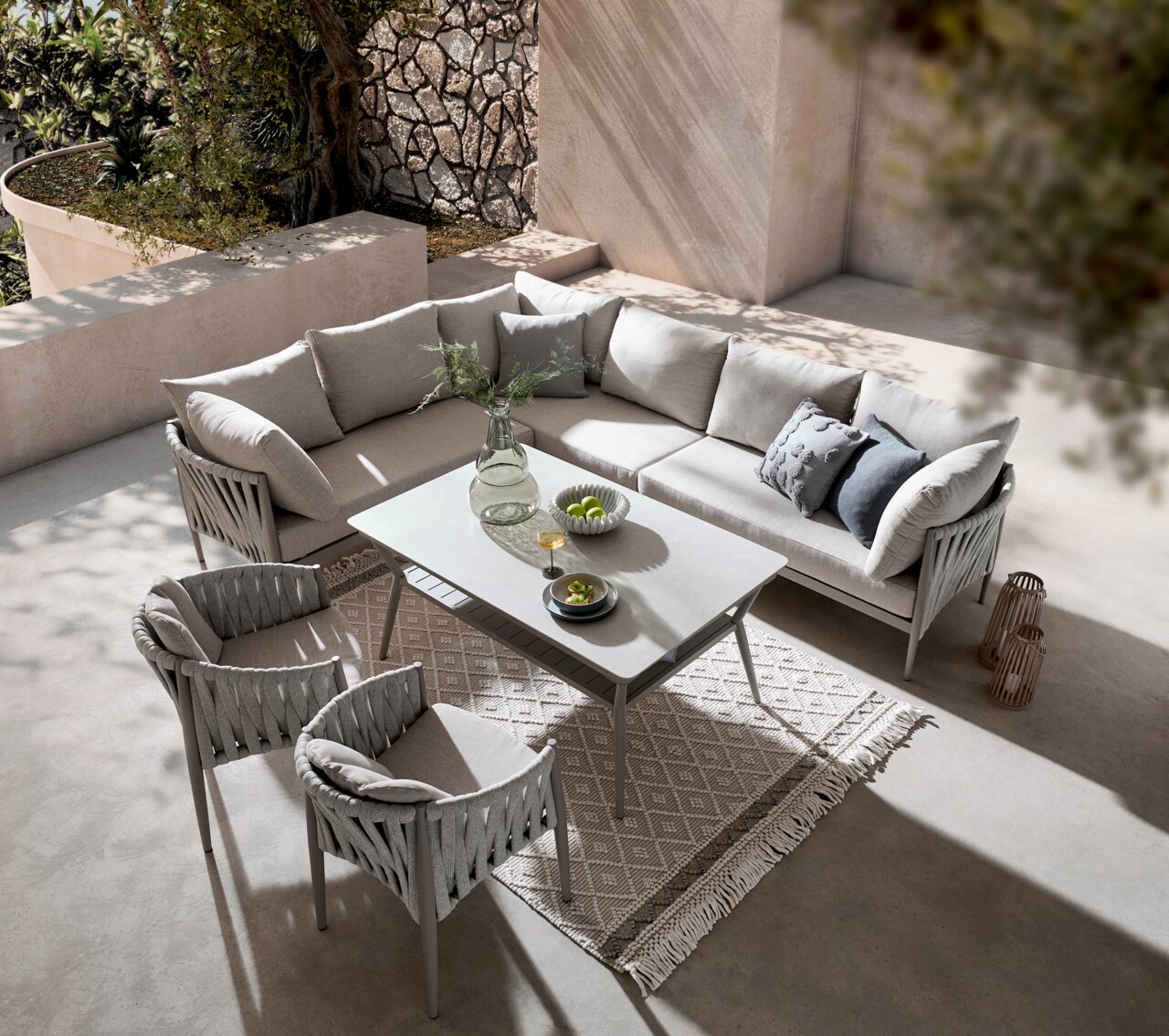 Moderner Gartentisch mit grauen Stühlen und einem Ecksofa in einer stilvollen Terrasse, von oben betrachtet.