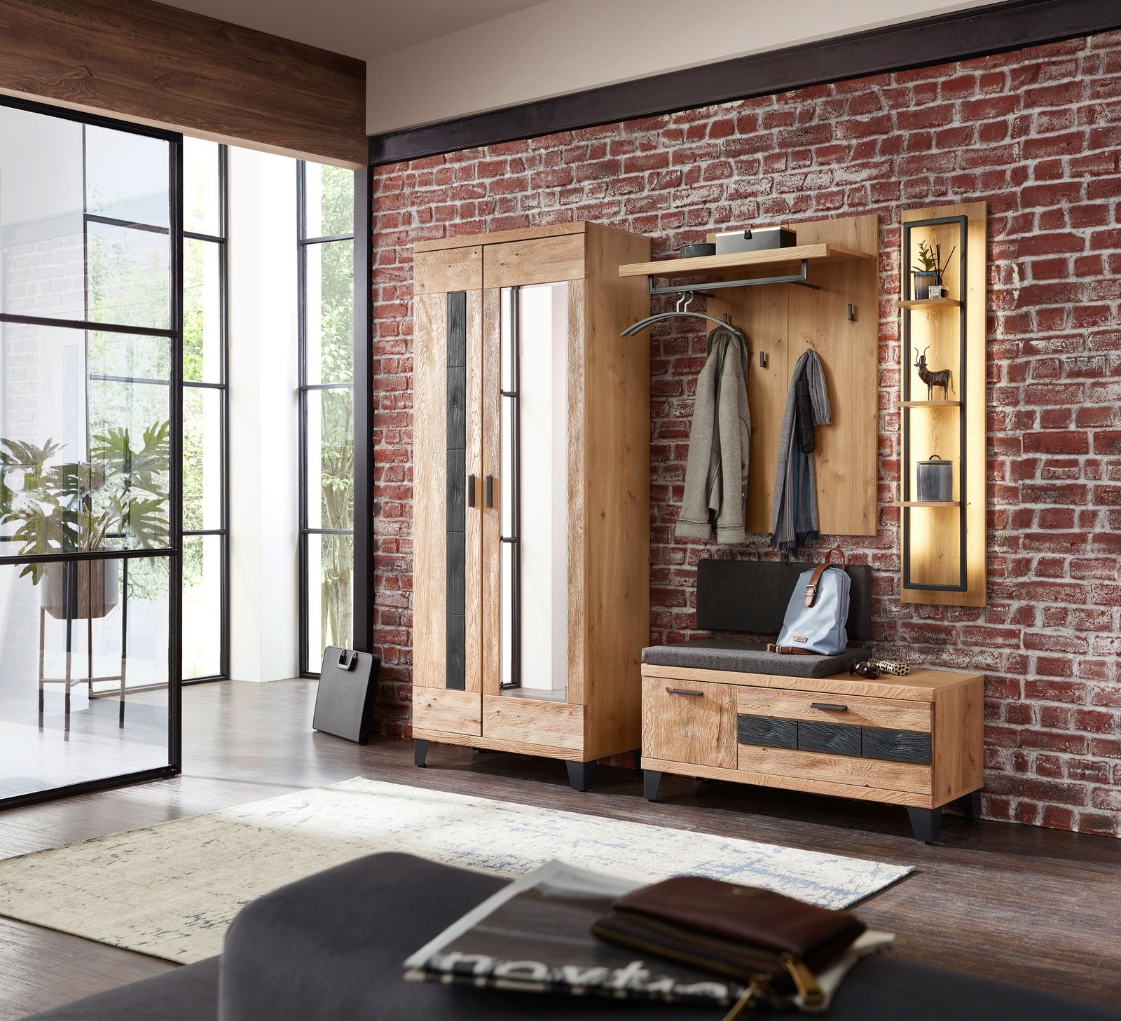 Garderobenkombination Set 81 in einer modernen Wohnung mit Backsteinwand, bestehend aus einem Schrank, einer Sitzbank mit Stauraum und einer Wandgarderobe, aus Holz mit Metallakzenten, seitliche Perspektive.