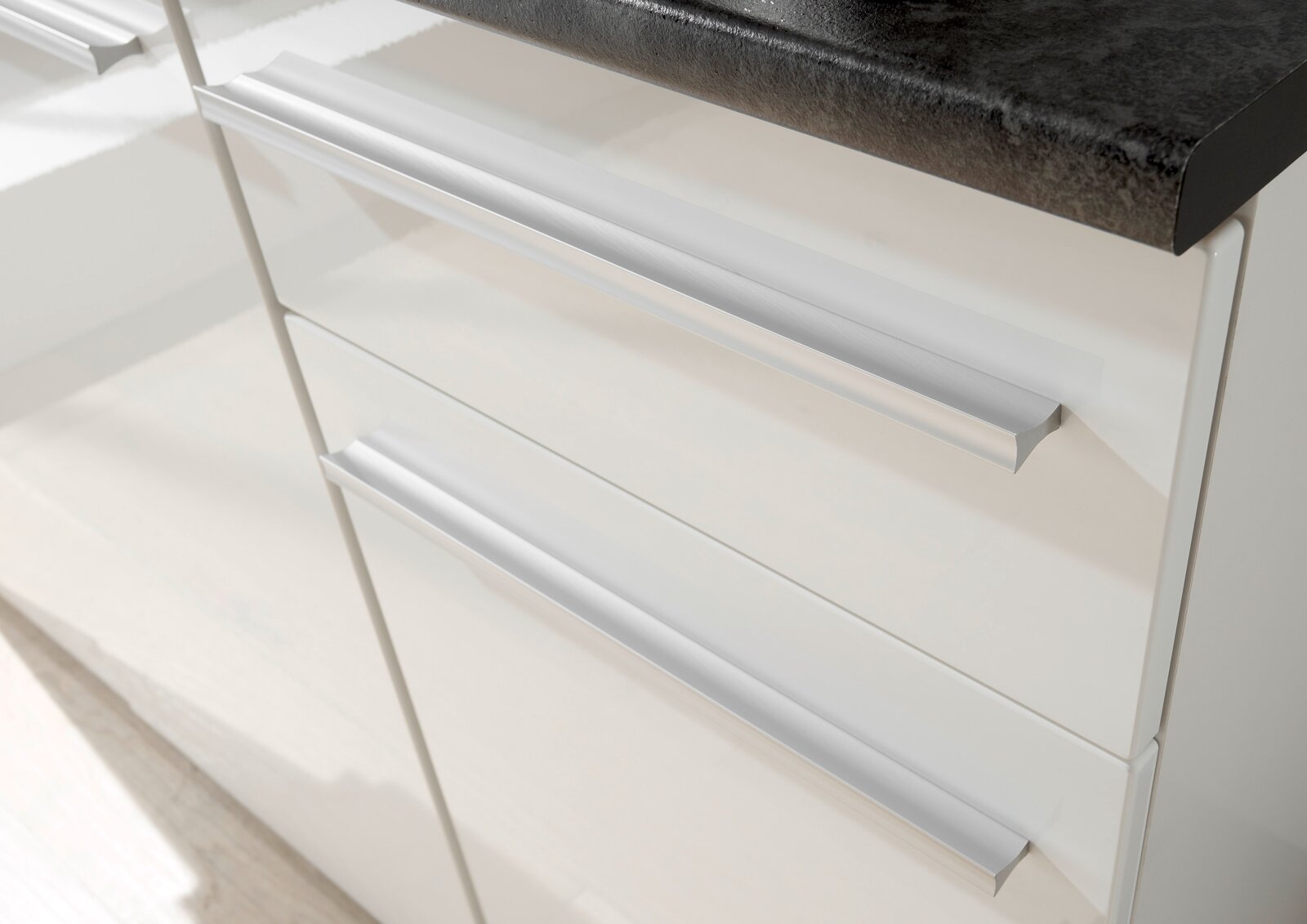 Nahaufnahme von weißen Küchenschubladen mit silbernen Griffen, Ansicht von schräg oben.