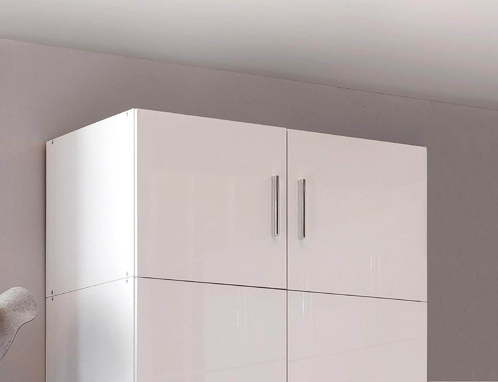 Weißer, glänzender Schrankaufsatz mit zwei Türen und silbernen Griffen, seitliche Perspektive.