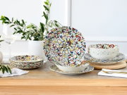 Bunt gemustertes Geschirrset aus Keramik/Porzellan mit floralen Ornamenten (Teller und Schalen) auf Holztisch dekorativ arrangiert, Perspektive: frontale Tischansicht auf Augenhöhe mit leichtem Blick von vorn.